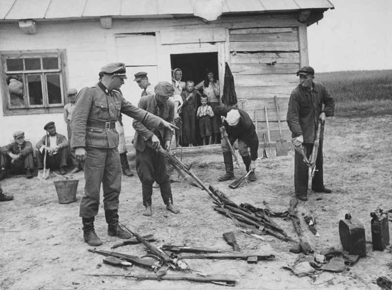 Жители деревни ломают собранные советские винтовки под контролем офицера СС.
