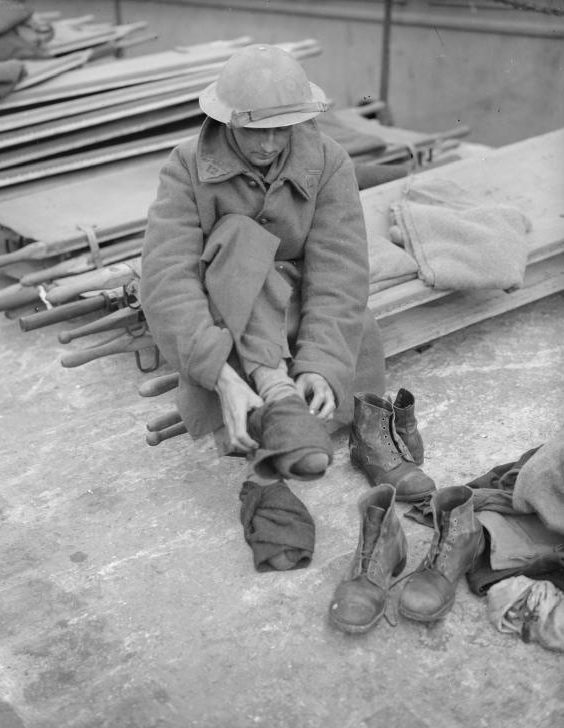 Эвакуированный солдат, одетый во французское пальто, меняет свои носки и ботинки. Довер, 31 мая 1941 г.