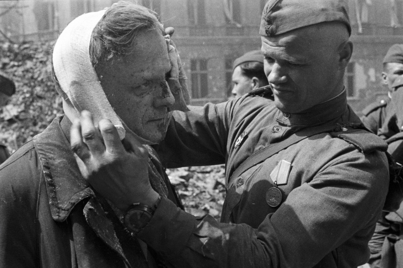 Советский солдат делает перевязку раненому берлинцу. Май 1945 г.
