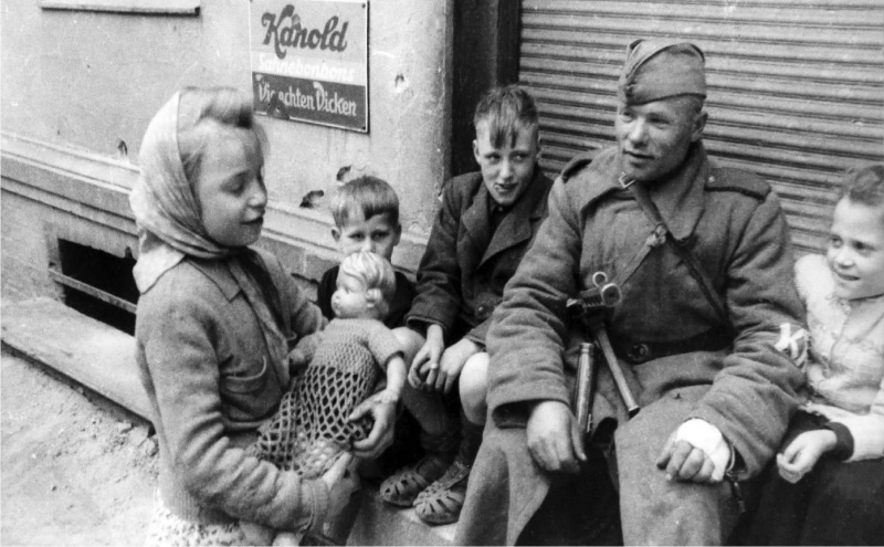 Красноармеец с немецкими детьми у входа в магазин. Май 1945 г.