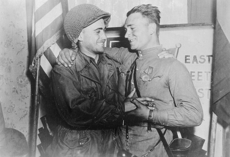 2-й лейтенант У. Робертсон и лейтенант А. С. Сильвашко на фоне надписи «Восток встречается с Западом», символизирующей историческую встречу союзников на Эльбе. 27 апреля 1945 г.