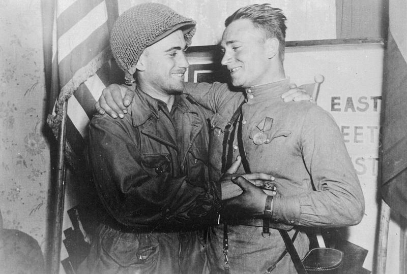 2-й лейтенант У. Робертсон и лейтенант А. С. Сильвашко на фоне надписи «Восток встречается с Западом», символизирующей встречу союзников на Эльбе. 25 апреля 1945 г.