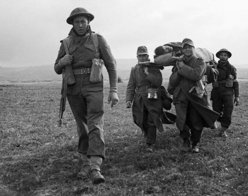 Немецкие военнопленные помогают нести раненого британского солдата у города Пишон. 8 апреля 1943 г.