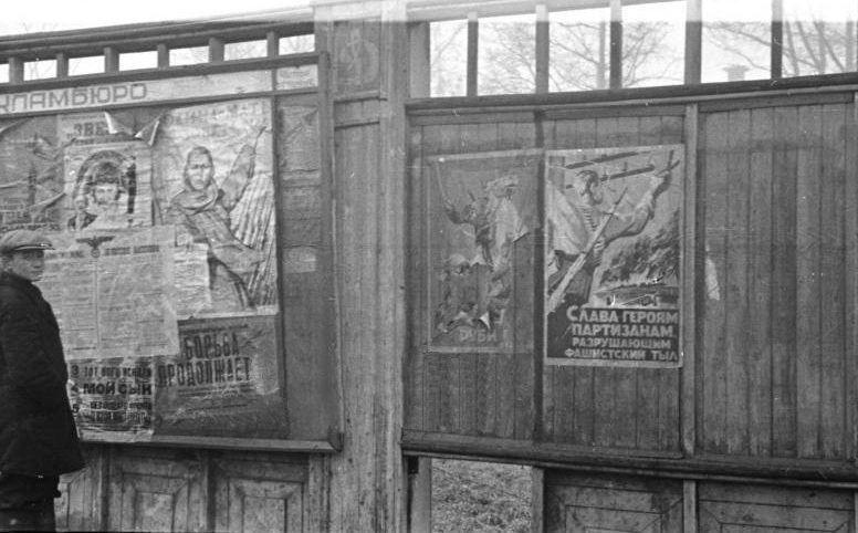 Местный житель у информационного стенда возле стадиона «Динамо». Приказы оккупационных властей наклеены на советские агитационные плакаты. Октябрь 1941 г. 