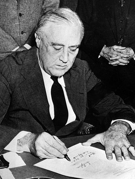 Президент Рузвельт, с траурной повязкой на рукаве, подписывает Декларацию о войне с Японией.