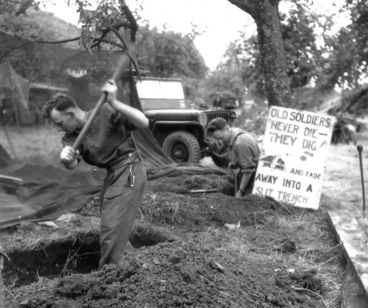Канадцы роют оборонительные окопы и щели в Нормандии. На щите написано: «Старые солдаты никогда не умирают — они роют окопы и исчезают в щелях». 25 июня 1944 г. 