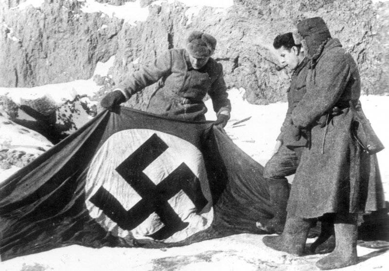 Советские бойцы рассматривают нацистский флаг на берегу Волги. Февраль 1943 г.