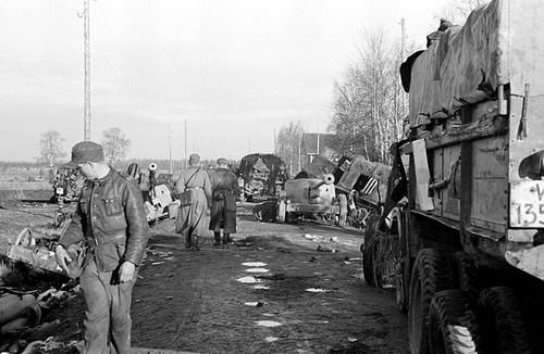 Финские военные осматривают колонну немецких автомобилей с артиллерийскими орудиями, уничтоженными и брошенными на сельской дороге. 1944 г.