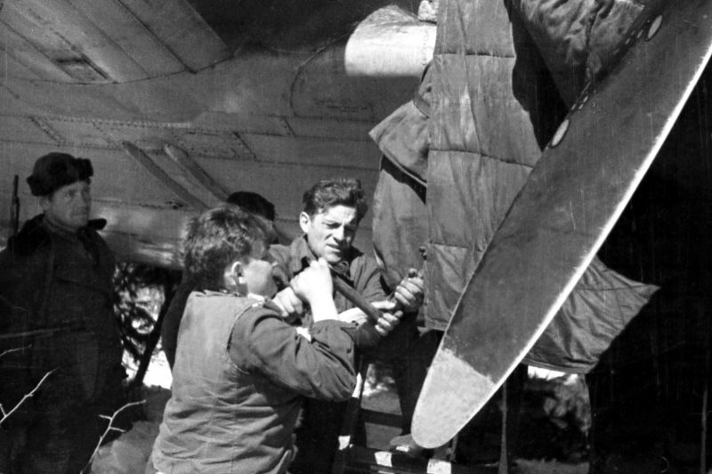 Члены экипажа самолета Ли-2 запускают двигатель самолета, находясь в расположении партизанского отряда. 1943 г. 