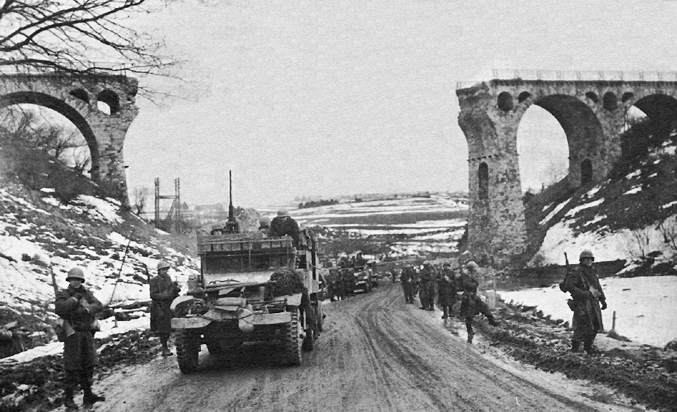 1-й батальон 26-го пехотного полка США проходит через железнодорожный виадук к северу от Бютгенбаха, Бельгия. Январь 1945 г.