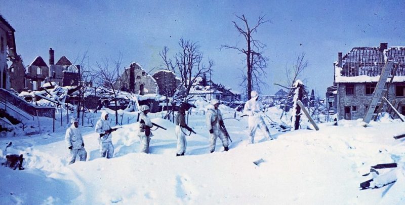 Солдаты белых маскхалатах идут по заснеженным улицам Сент-Вит, Бельгия. Январь 1945 г.