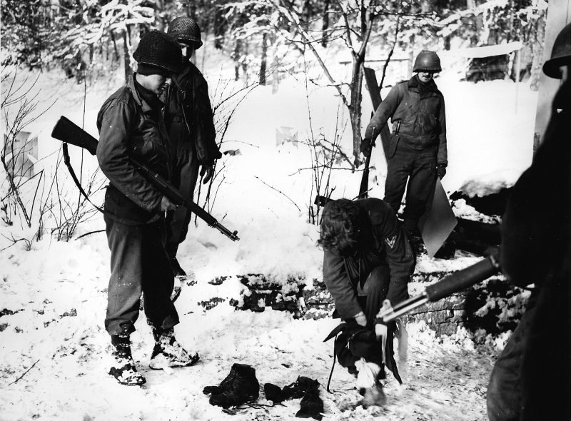 Американцы охраняют немецкого диверсанта, снимающего с себя американское обмундирование. Январь 1945 г.