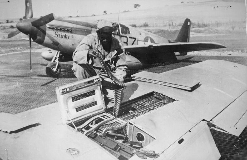 Оружейники загружают пулеметную ленту для крыльевых пулеметов истребителя P-51B «Мустанг». Сентябрь 1944 г. 