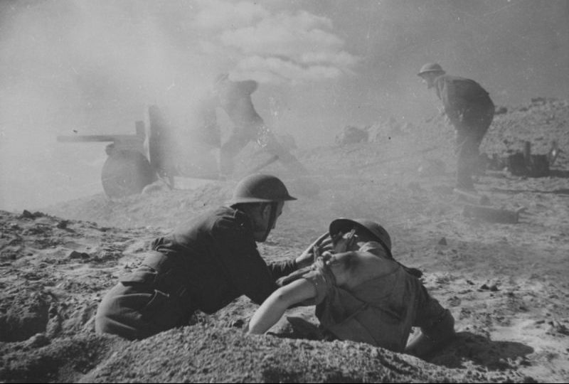 Британский солдат оказывает первую помощь раненому артиллеристу во время боя в Триполитании. Декабрь 1942 г.
