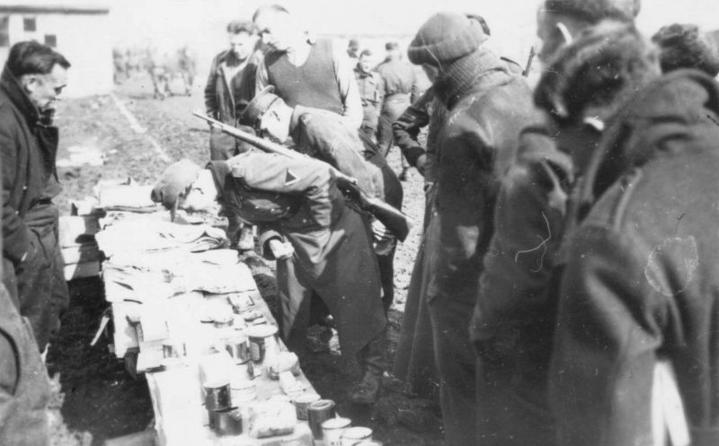 Немецкий солдат-конвоир на рынке концлагеря «Шталаг 383» в окружении пленных союзников. 1943 г. 