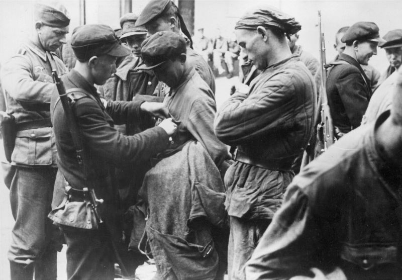 Немецкий унтер-офицер и члены «Самообороны» обыскивают пленных красноармейцев в Таллине. Сентябрь 1941 г. 