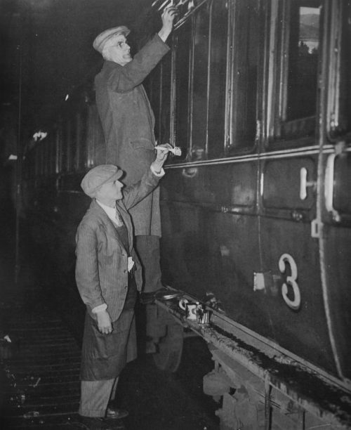 Рабочие закрашивают окна пригородного поезда в целях светомаскировки на вокзале в Лондоне. 1940 г.
