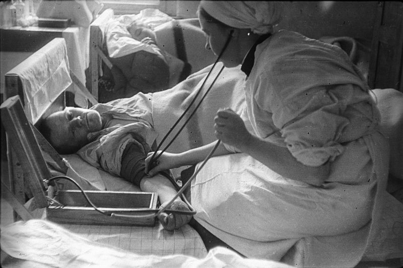 Медсестра в госпитале измеряет давление красноармейцу, раненому во время штурма Берлина. Апрель 1945 г. 